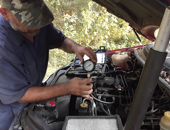 Mechanic using a pressure gauge to inspect a car engine under the hood for shock absorber replacement services in Harrisburg, NC.