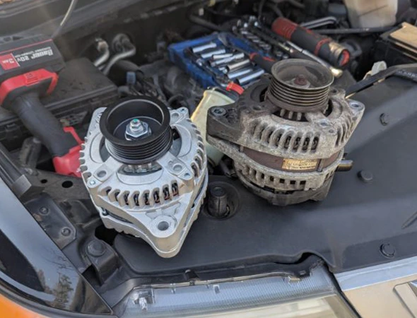 Comparison of a new and old car alternator sitting on an engine block during a cooling system and radiator repair service.