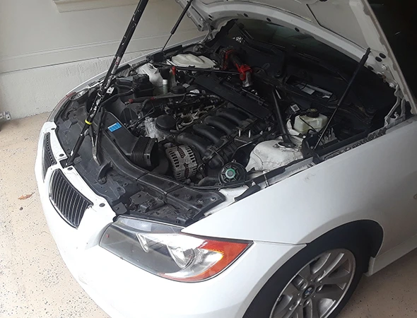 Open hood of a white BMW showing the engine bay during an expert water pump installation service in Huntersville, NC.